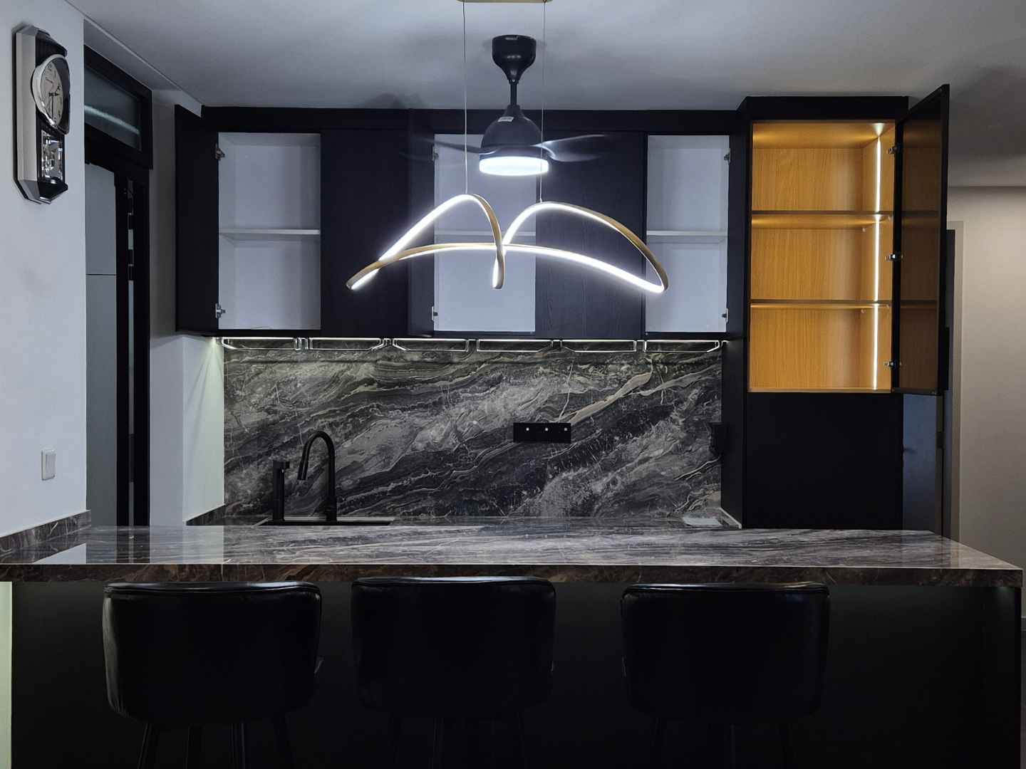 Black modern kitchen with marble backsplash, pendant light, and backlit display cabinet